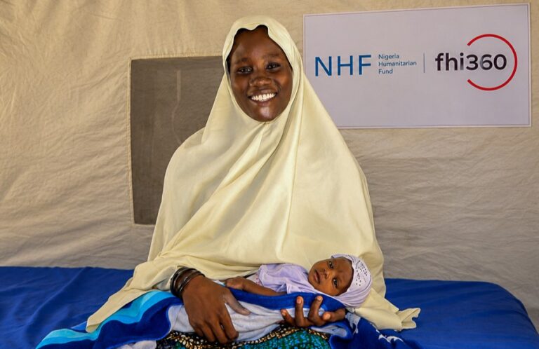 A smiling woman wearing light yellow holds her newborn baby.